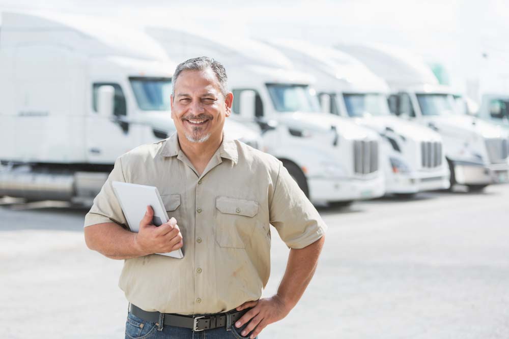 Photo of a Fleet Manager standing in front of four Semi-Trucks
