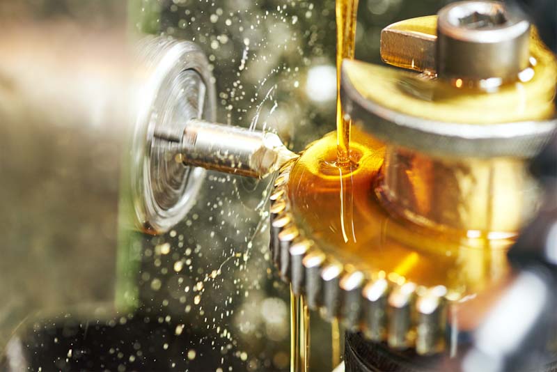 Photo of an industrial tooth gear wheel machining with oil being poured onto it.