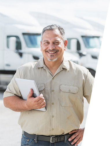 Photo of fleet manager smiling at camera and standing in front of trucks.